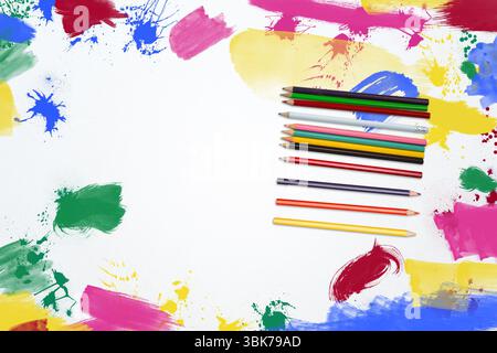 Colored pencils are lying on white surface in flat design with paint splatters and brush strokes Stock Photo