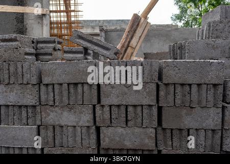 Pile of gray bricks with a wooden stick leaning on them. The bricks are stacked in a way that they are leaning on each other, creating a sense of inst Stock Photo