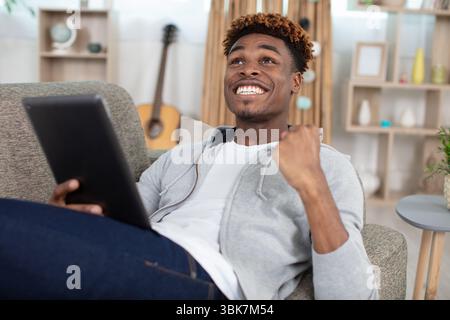 man with tablet in the living room celebrating a victory Stock Photo