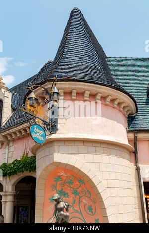 Exterior view of Auberge de Cendrillon restaurant with a conical roof, sign, and statue. Soft pink and peach hues dominate the architecture  at Disney Stock Photo