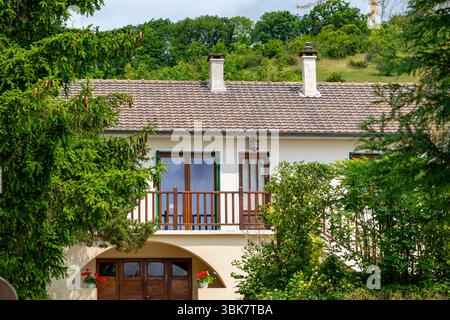 Two-story house with tile roof, fronted by greenery. A small balcony is visible, with trees on either side in Giverny, France. Stock Photo