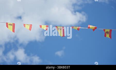 Flags of spain wave against a sunny blue sky outdoors in a vibrant display of national pride and celebration. Stock Photo