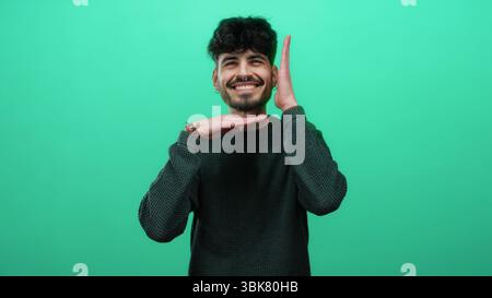 Young hispanic man smiling in front of an isolated green background performing a time-out gesture showcasing his casual style. Stock Photo