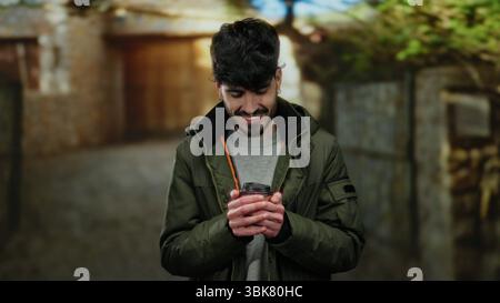 Young man in urban setting holding coffee cup, dressed warmly outdoors, showcasing style and warmth on a city street. Stock Photo