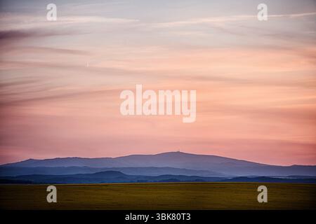 Vibrant pink and purple sunset sky over misty, layered mountain silhouettes and open fields. Stock Photo