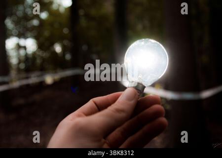 A hand holds a brightly glowing light bulb against a dark background, symbolizing innovation, creativity, and new ideas. Stock Photo