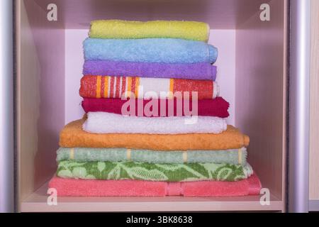 multicolored towels on the shelves in the wardrobe. Stack of towels . Stock Photo