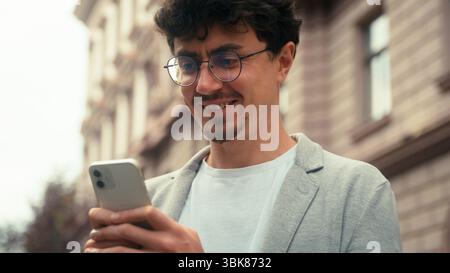 Smiling Hispanic ethnic business man positive carefree businessman male guy employer entrepreneur in city street outdoors holding mobile phone using Stock Photo