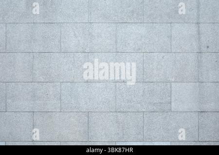 A full-frame, detailed view of a wall constructed from rectangular, light gray granite tiles. Stock Photo