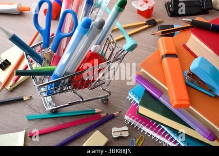 School supplies shopping concept with a mini shopping cart filled with pencils and other various school tools and materials around on a wooden table a Stock Photo