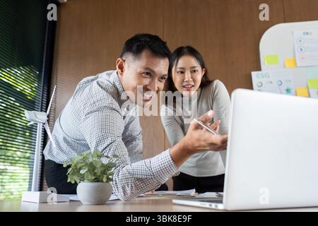 Collaborative Strategy. Two professionals discussing ESG initiatives over a laptop in a modern office. Stock Photo