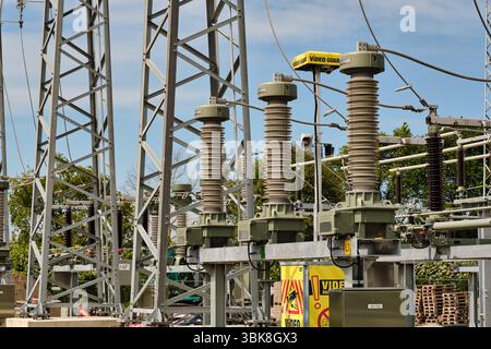 June 18, 2025 - Karlshagen‑Germany: Three  phase insulators dominate the foreground of the new substation site, with a yellow mobile security camera o Stock Photo