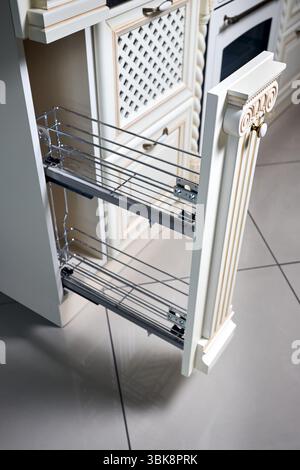 Pull out spice rack cabinet filler pantry. Interior of modern kitchen in classic style with golden elements in beige colors. Vertical drawer for spice Stock Photo