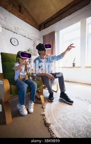 Father and child exploring virtual reality with VR headsets in bright modern living room setting Stock Photo