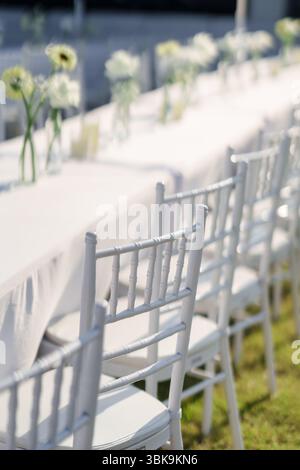 Elegant outdoor wedding long table with candle, white rose flower and white chairs in the garden on marriage festive Stock Photo