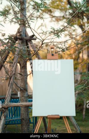 Blank white canvas set on wooden easel placed front of wedding event in natural environment and soft garden in rustic style Stock Photo