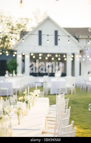 Elegant outdoor wedding long table with candle, white rose flower and white chairs in the garden on marriage festive Stock Photo