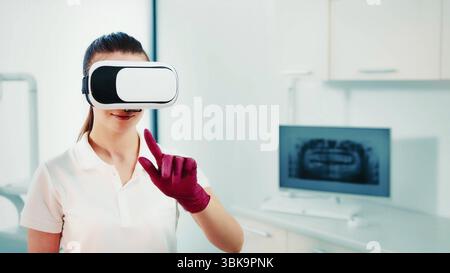 Dental professional using virtual reality in a clinic. A young dental professional wearing virtual reality goggles and red gloves interacts with a Stock Photo