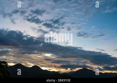 Dramatic Sunrise Over Mountain Silhouettes Beneath Dynamic Cloudscape Stock Photo