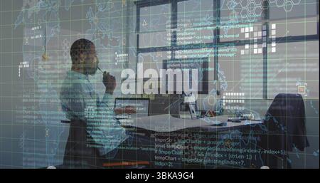 Analyzing code and map overlay on dual monitors in office, African American engineer holding pen. Technology, professionalism, innovation, data, analy Stock Photo