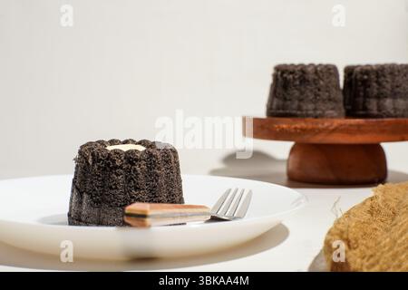 A single portion of black glutinous rice bundt cake with cheese center, placed on a ceramic plate with fork and spoon. Classic homemade dessert Stock Photo