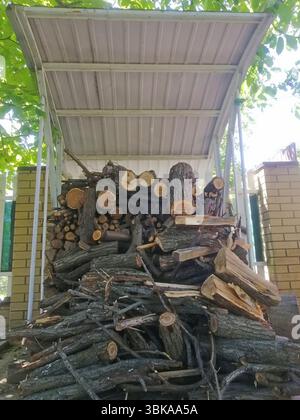 vertical photo Rustic pile of firewood under corrugated roof near fence, tree shadow covering ground, logs waiting for use, outdoor scene evokes calmn Stock Photo
