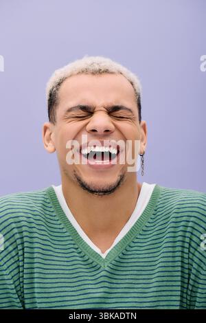 A joyful young Black man laughs in a stylish outfit, surrounded by purple. Stock Photo