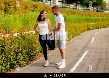 In a lively park, a fitness trainer assists a woman in stretching to enhance flexibility and promote an active lifestyle amidst lush greenery. Stock Photo