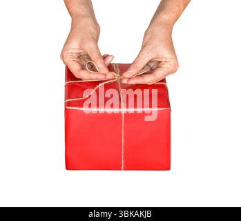 Closeup woman's hands wrapping present in red gift paper tying with twine string isolated cutout on white Stock Photo