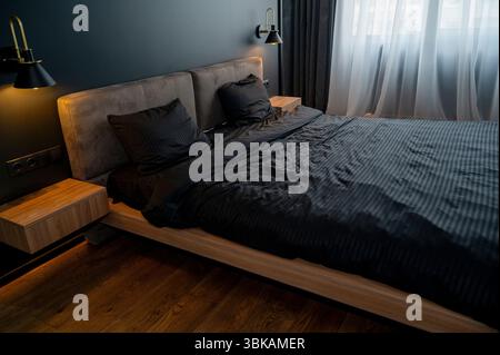 Modern bedroom with double bed in dark interior. On the bed there is black bed linen Stock Photo