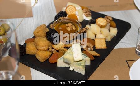 Cheese platter with honey, dried fruits, crackers, and nuts on a black slate background, representing gourmet appetizer concept Stock Photo