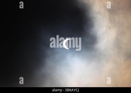 Solar eclipse partially obscured by dramatic clouds, creating a surreal celestial scene in the sky. Stock Photo