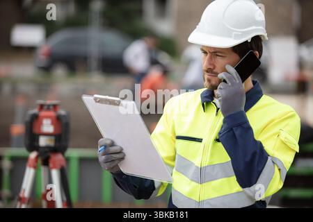 contractor on site looking at clipboard and talking on smartphone Stock Photo