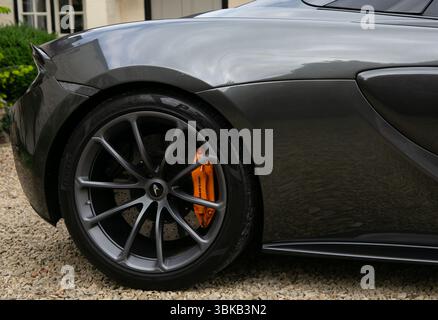 Close-up view of a luxury sports car's rear wheel with orange brake caliper parked on a gravel driveway Stock Photo