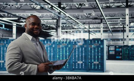 Data center software developer using tablet to do AI algorithms improvements. Programmer in server hub using laptop, maintaining databases supporting artificial intellgience applications, camera A Stock Photo