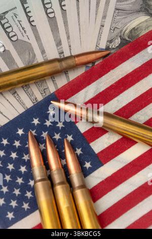 Close-up of firearm ammunition lying on an American flag with blurred dollar notes in the background. The image symbolises the themes of war, security Stock Photo