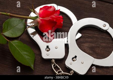 still life depicting a red rose and metal handcuffs on a dark wooden background. The composition symbolises the contrast between love and coercion, fr Stock Photo