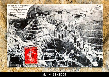 An old postcard with a motif from Coussac-Bonneval shows the extraction of kaolin. It hangs in the Musée du Four des Casseaux on Rue Donzelot in Limoges, Haute-Vienne, Nouvelle-Aquitaine, France. The caption reads "Coussac-Bonneval (Haute-Vienne) – Carrière de Marsse – Le Kaolin (Terre à Porcelaine) – Son extraction". In English: "Marsse quarry – kaolin (porcelain clay) – its extraction". Men in hats and women in long skirts work on the stepped terraces of the pit, and wooden scaffolding stands in the foreground. At the top edge, horses stand next to a cart. A red 10-centime stamp is stuck on  Stock Photo
