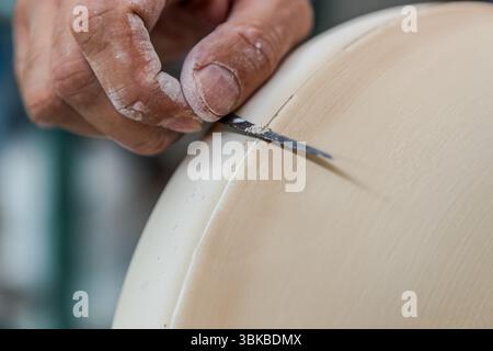 At the Ateliers Arquié art porcelain workshop on Avenue Baudin in Limoges, Haute-Vienne, Nouvelle-Aquitaine, France, a hand uses a narrow blade to remove the casting seam from the edge of a large, round piece. This step is known as fettling. Fine white dust clings to the fingers and the blade. The workshop was founded in 1996 and specialises in the design and production of customisable and artistically designed porcelain objects. It combines traditional craftsmanship with modern shapes, colours and techniques. It works with around 15 different artists. Pharmacy porcelain used to be produced on Stock Photo