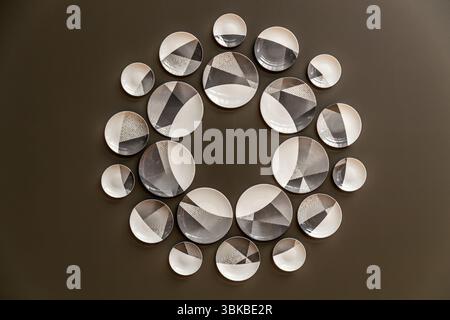 A modern porcelain series decorates a wall of the Musée National Adrien Dubouché on Place Winston Churchill in Limoges, Haute-Vienne, Nouvelle-Aquitaine, France. Around 20 white plates of various sizes hang in a circle on a dark brown wall. Their decoration consists of grey and black triangular areas with fine grid and dot patterns. The museum was founded in 1845 as the city's first museum. Adrien Dubouché, a patron of the arts and son of a cloth merchant, took over its management in 1865. He greatly expanded the exhibition through generous donations and the acquisition of important ceramic co Stock Photo