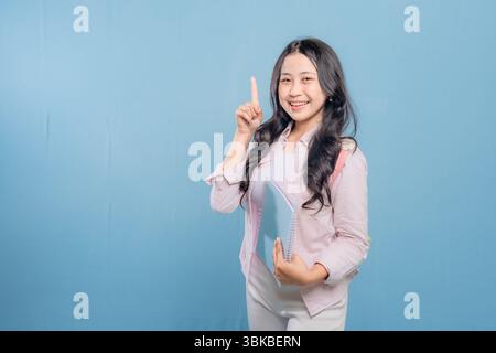 A woman is holding a blue book and pointing to something important. She is smiling and she is happy Stock Photo