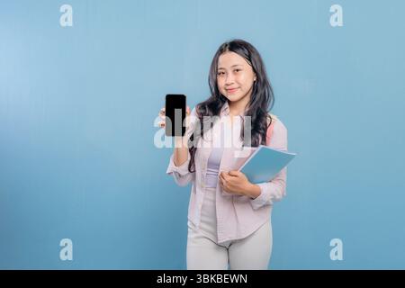 A woman is holding a cell phone and a stack of books. the woman wants to show the information on her cell phone Stock Photo