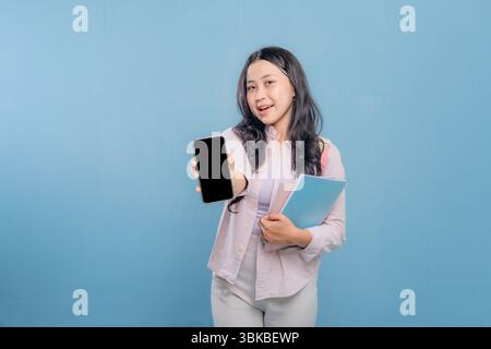 A woman is holding a cell phone and a stack of books. the woman wants to show the information on her cell phone Stock Photo