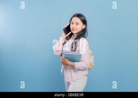 A woman is talking on her cell phone while holding a stack of books. She is smiling and she is in a good mood Stock Photo