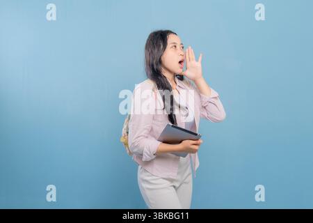 A woman is holding a tablet and is making a loud noise. She is wearing a pink shirt and white pants Stock Photo