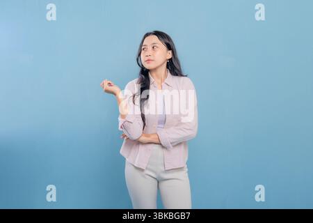 A woman in a pink shirt and white pants is looking up at the camera. She is thinking or pondering something Stock Photo