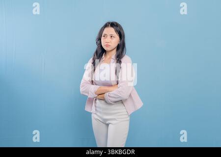 A woman in a pink shirt and white pants is standing with her arms crossed. She looks unhappy and is frowning Stock Photo