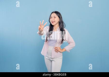 A woman is posing with her hands in the air, making a peace sign. She is smiling and she is happy Stock Photo