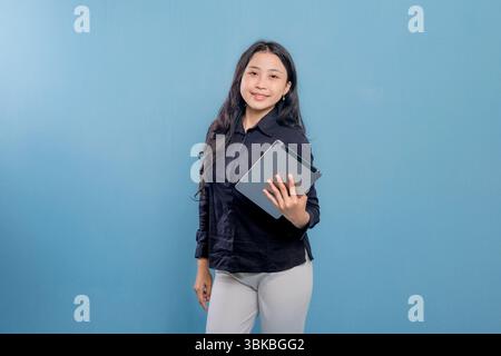 A woman is smiling and holding a tablet. She is wearing a black shirt and white pants. Concept of professionalism and confidence Stock Photo