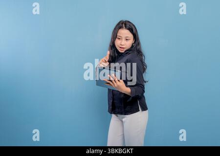 A woman is holding a tablet and giving a thumbs up. She is wearing a black shirt and white pants Stock Photo